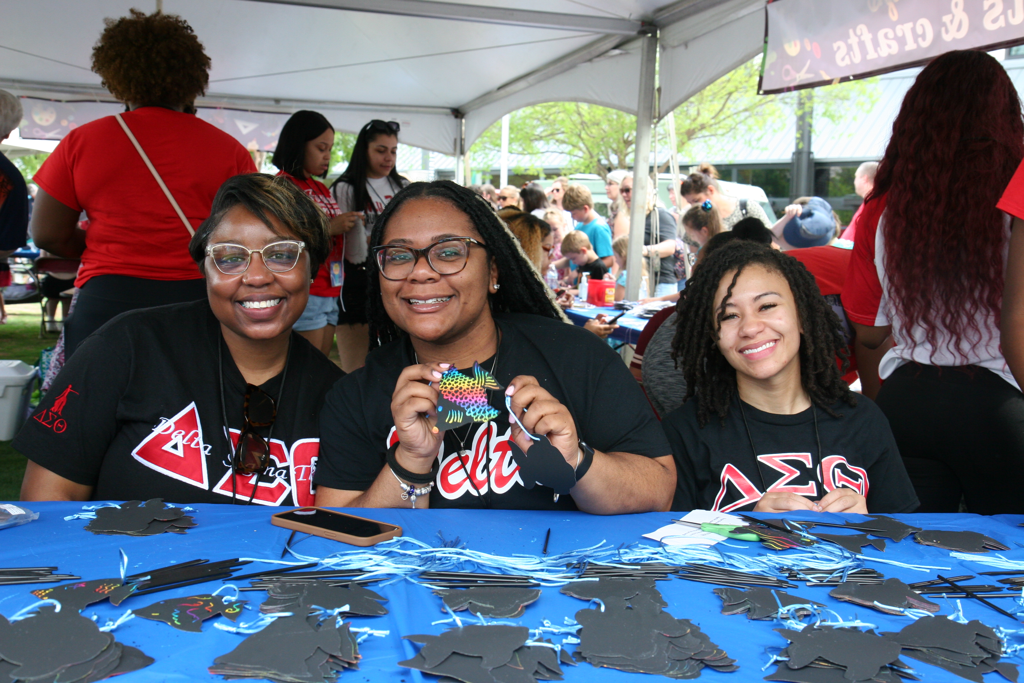 Photo of three smiling women at a table helping with kids crafts