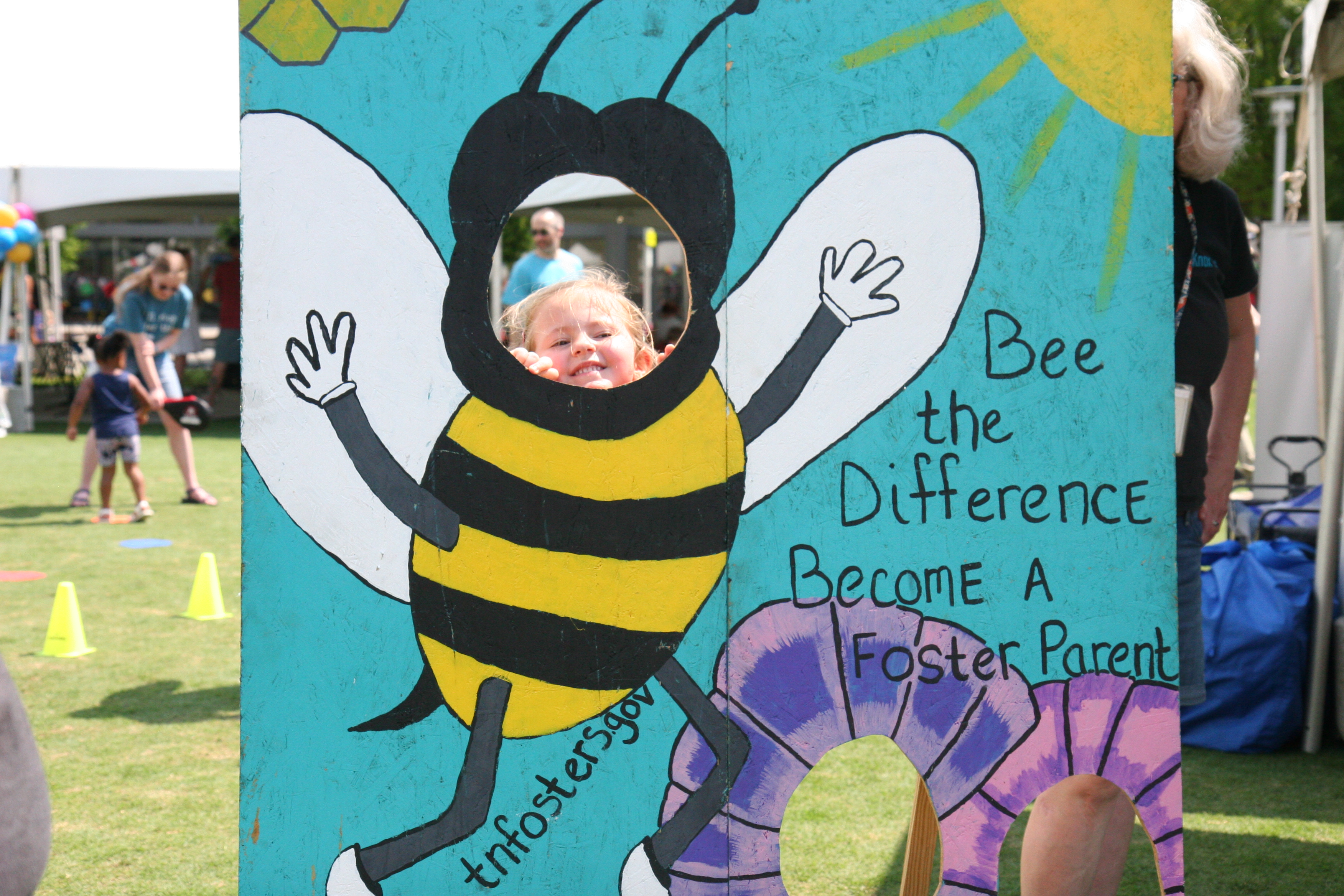 Small child peeks through a painted cutout of a bee