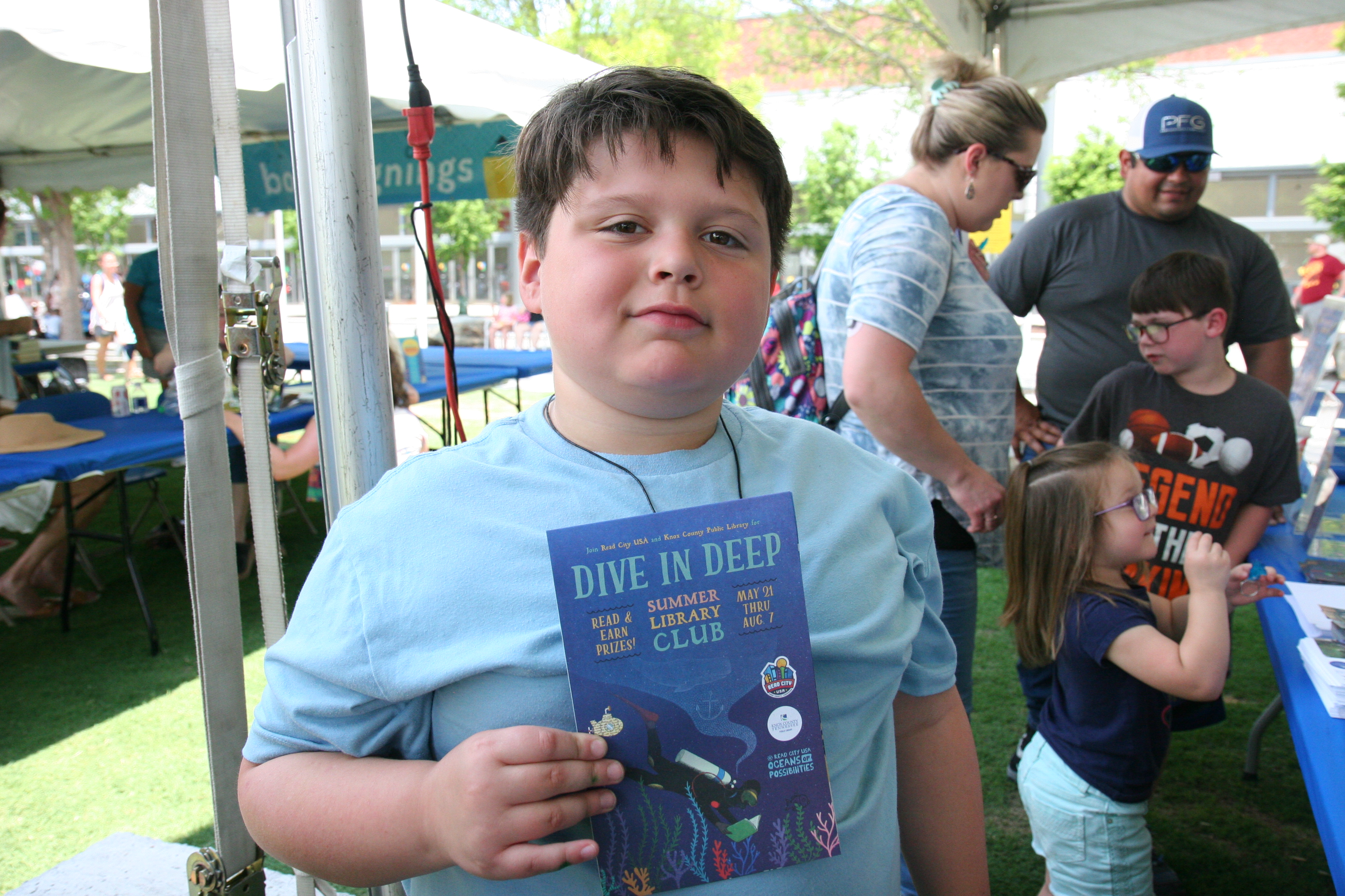 Boy holds a Summer Library Club map which reads Dive in Deep