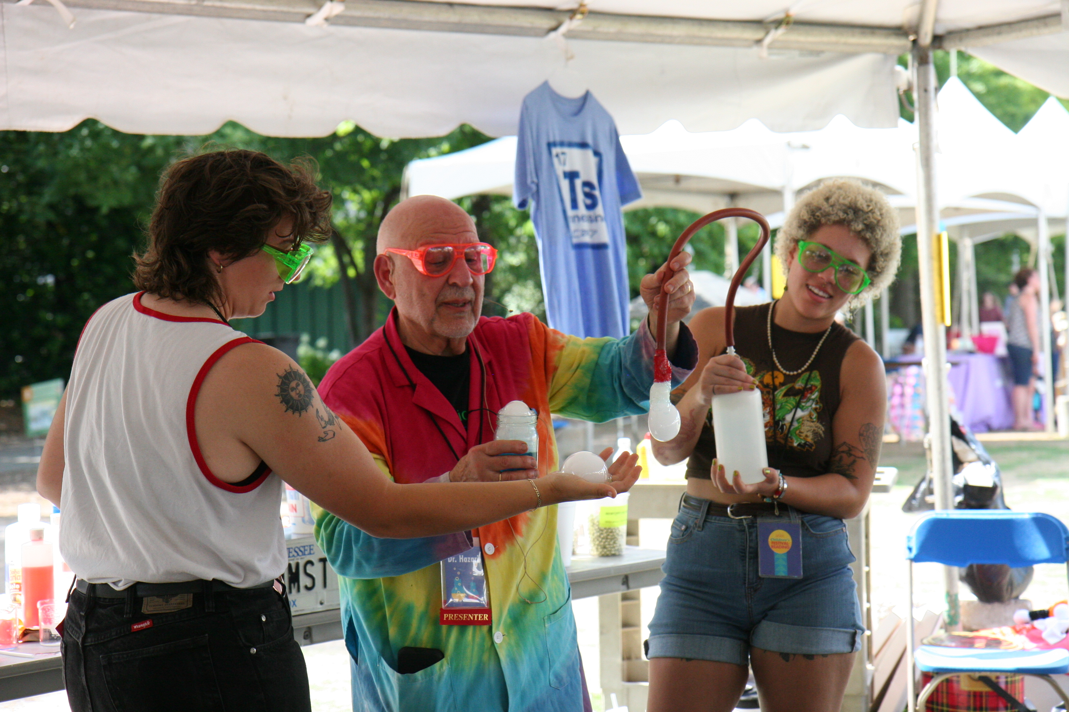 A presenter in a tie-dye lab coat with two assistants for a science experiment