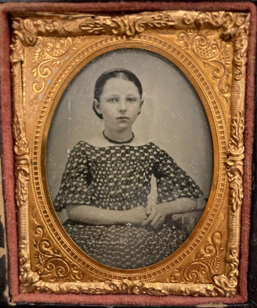 Black-and-white ambrotype of a young female seated with her hands in her lap.