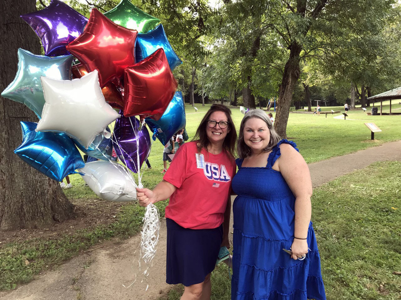 photo of two women smiling, one holds a large bundle of star-shaped helium balloons