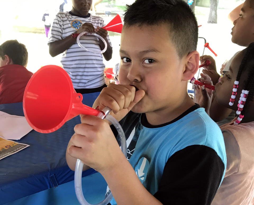 young boy plays a homemade trumpet made from a plastic funnel and tube