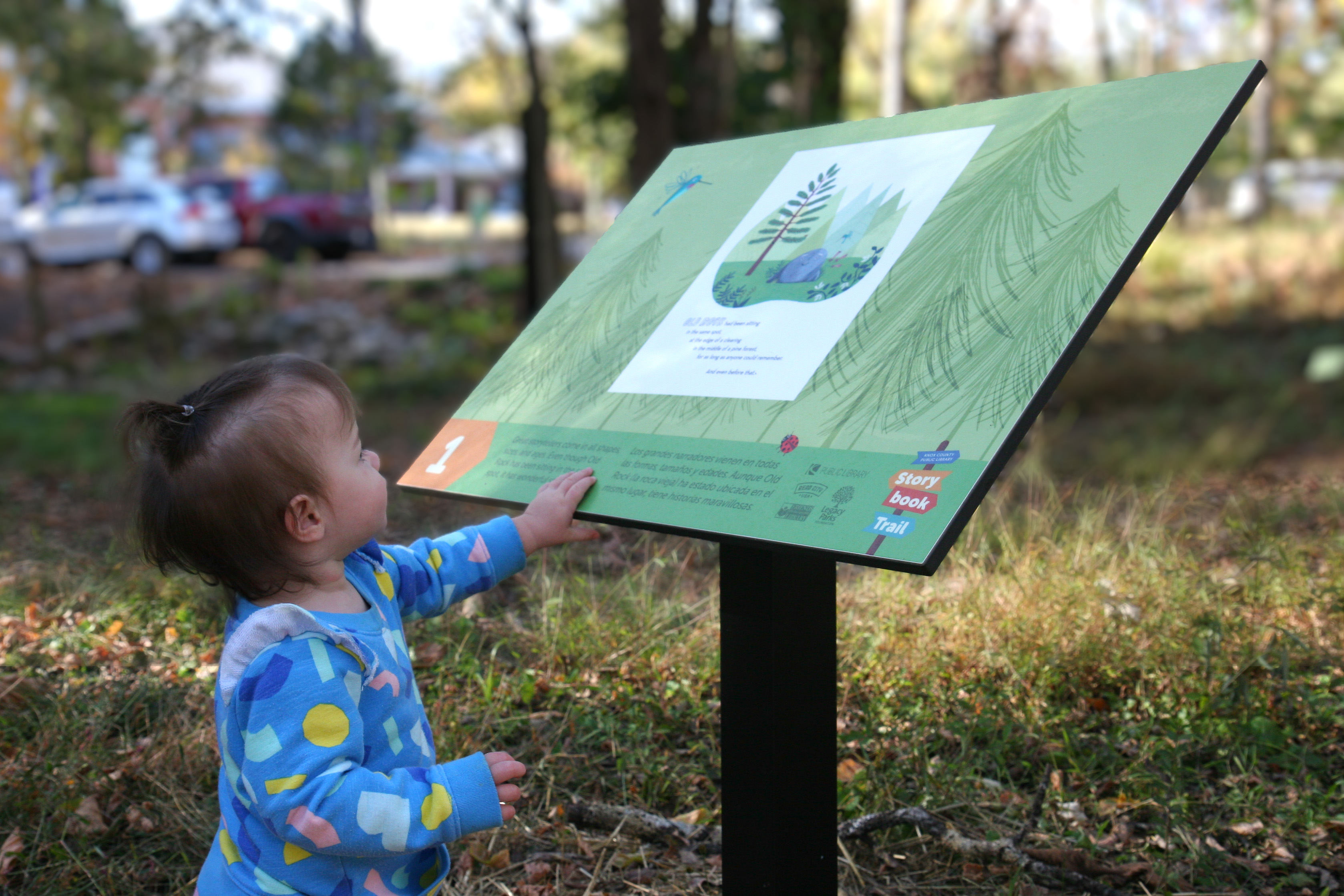 little girl reads a storybook trail panel