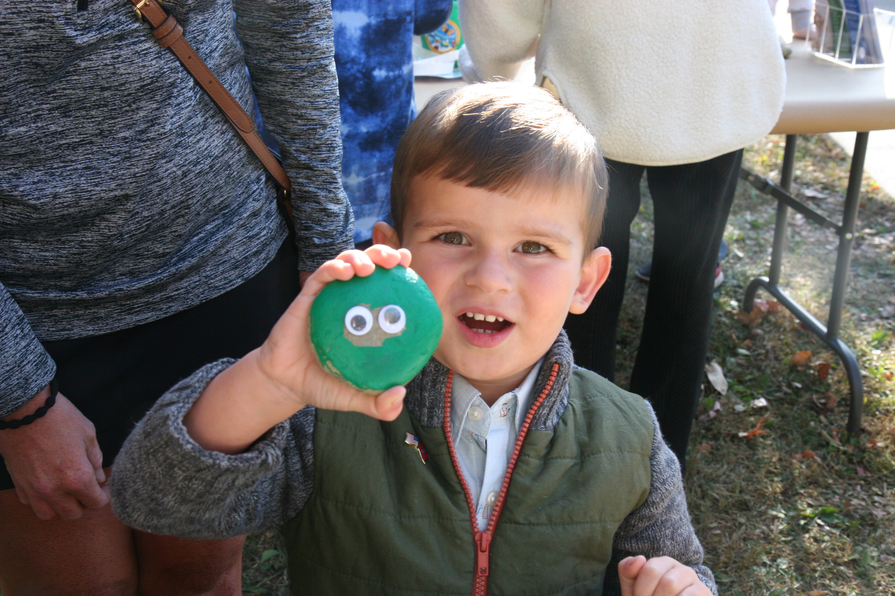 boy holds up green rock with googly eyes