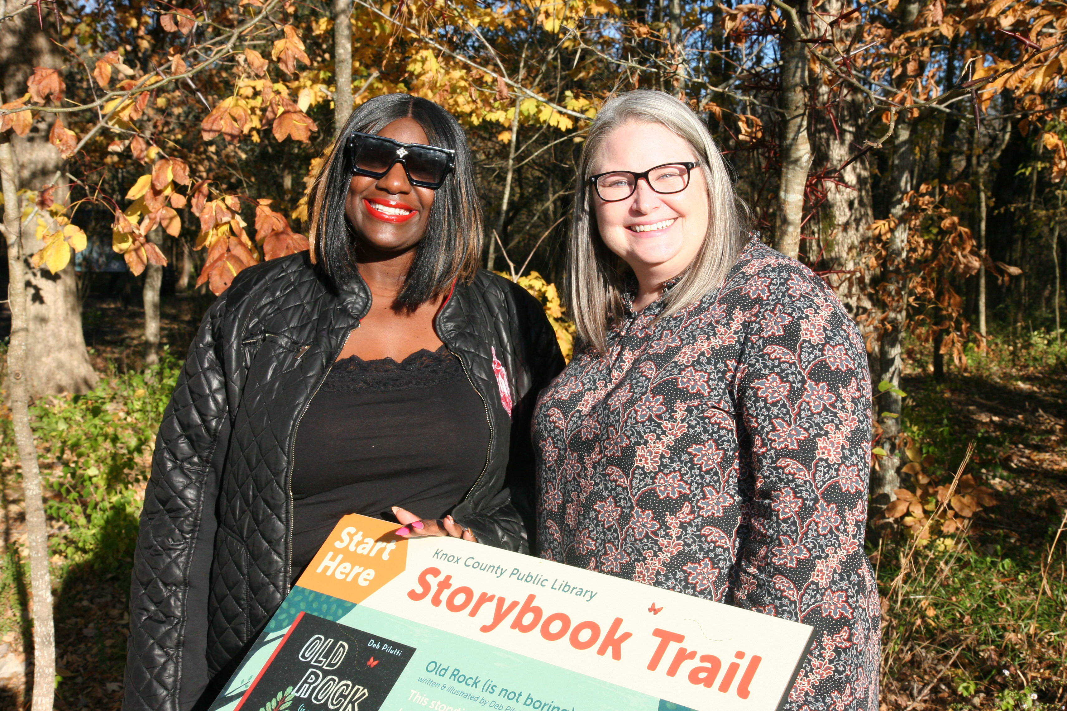 two women stand beside storybook trail panel