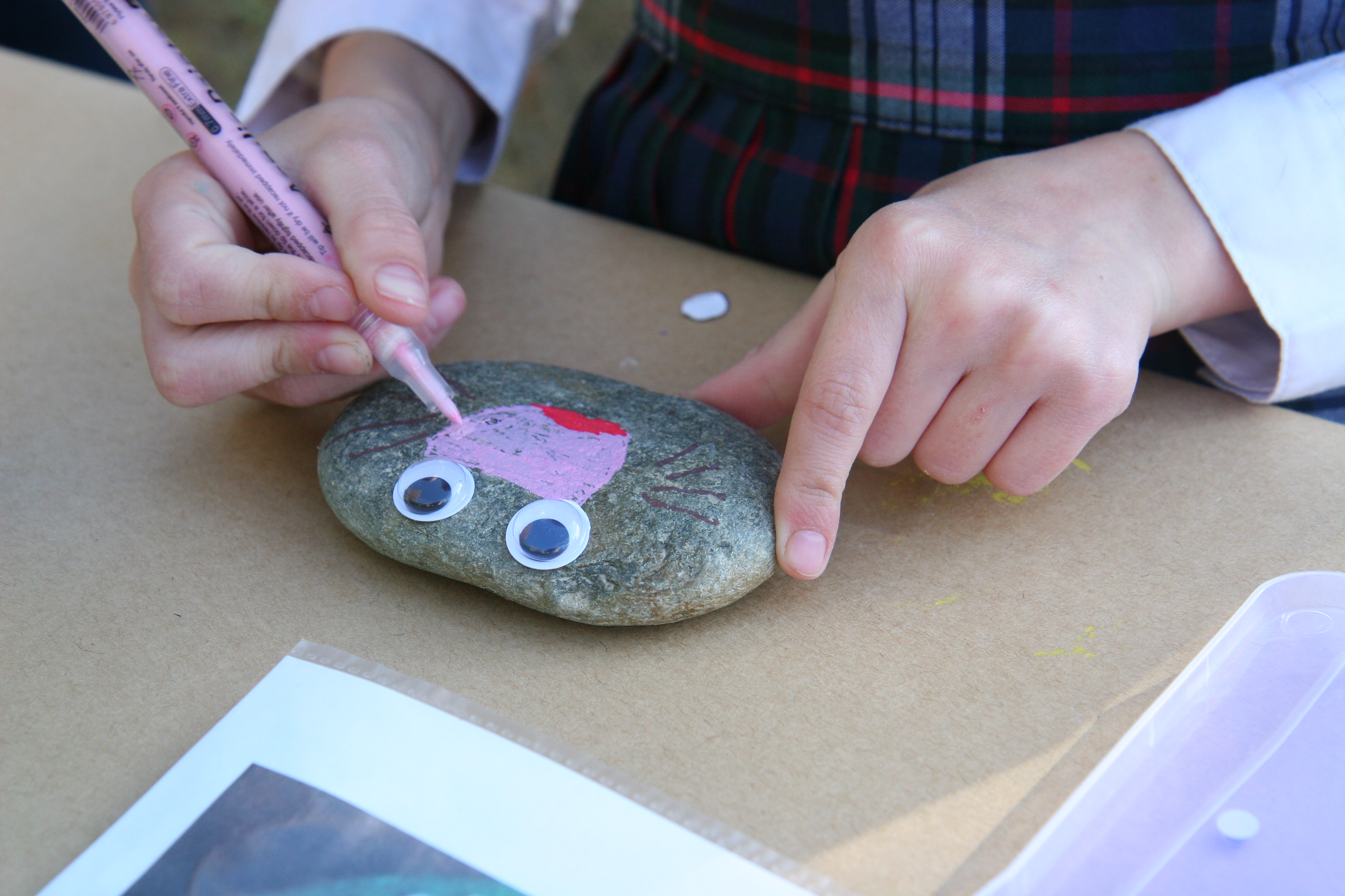 young girl paints a pink nose on a painted rock animal