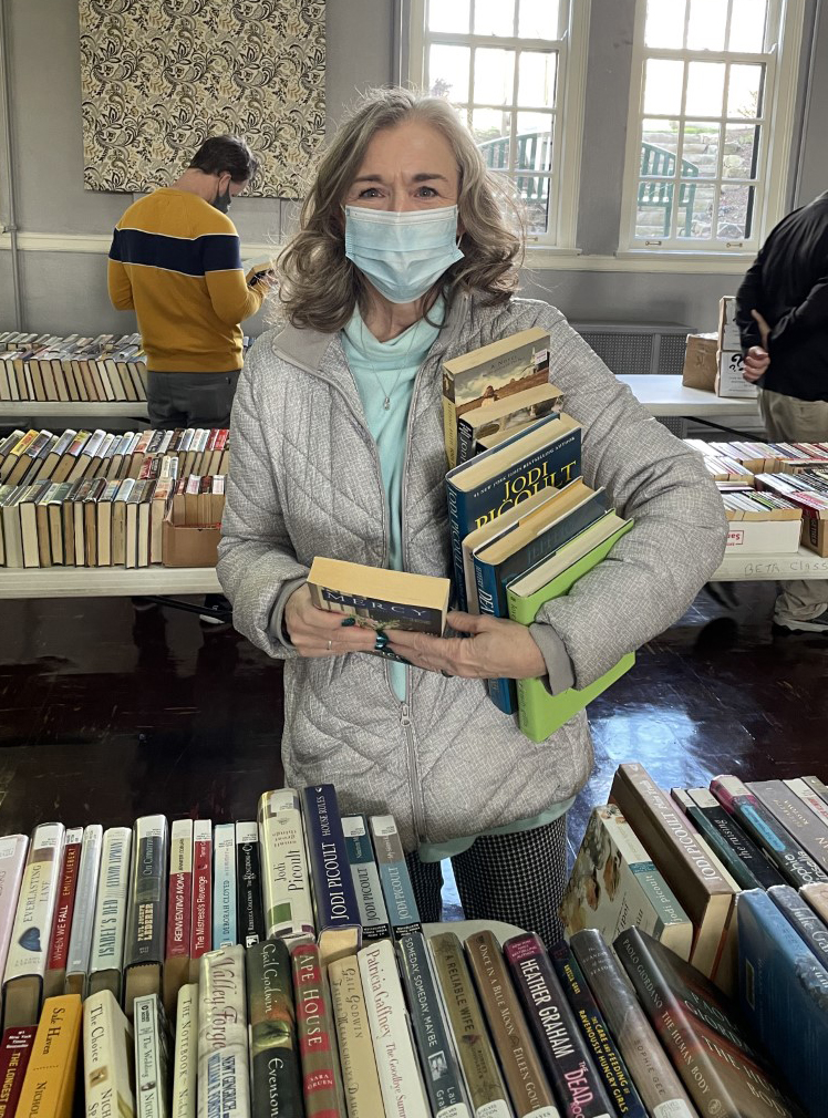 woman holding an armful of books in front of a table full of books