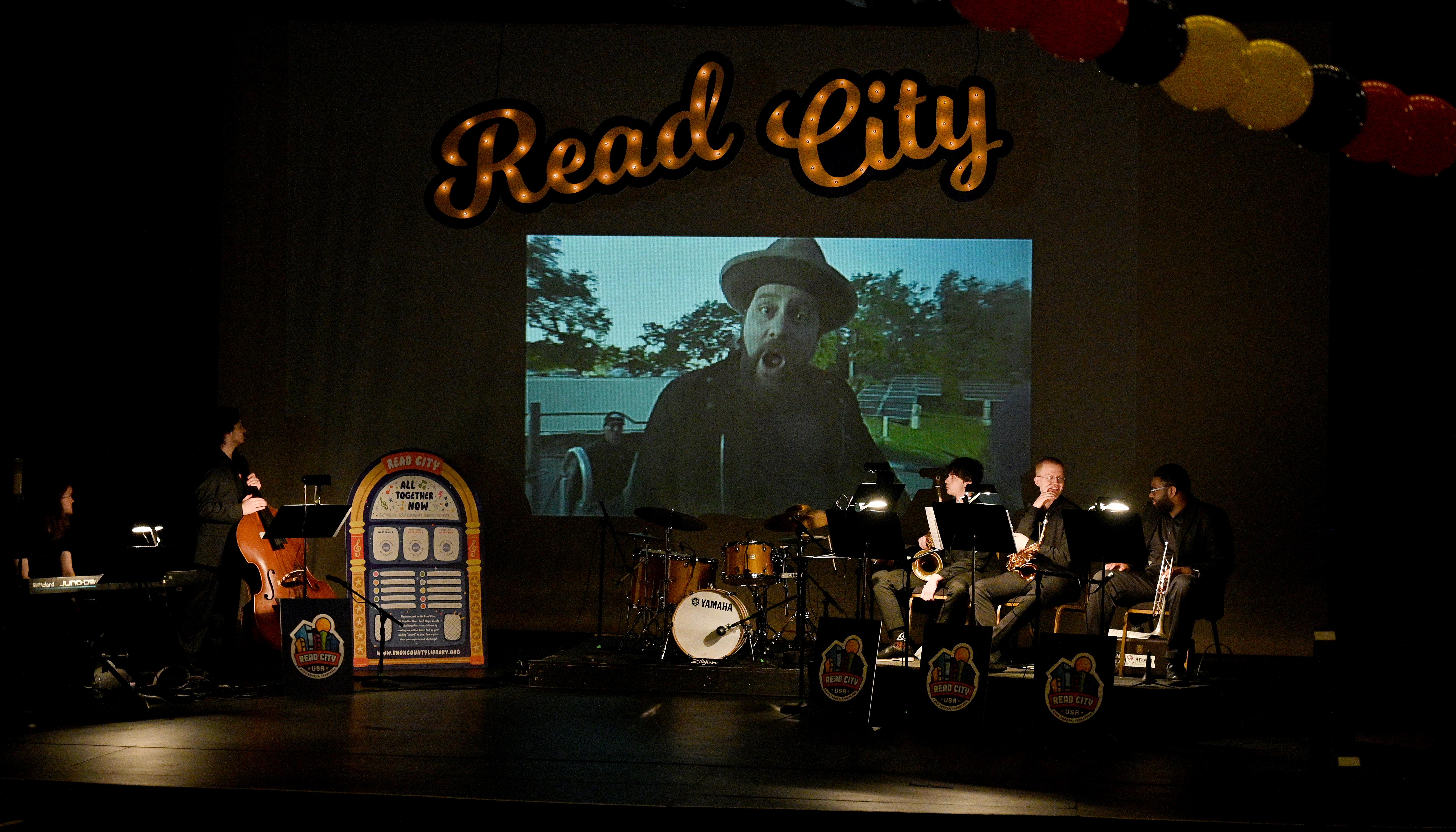 a stage with a small band, Read City in marquee letters, and a video screen showing an image of Coy Bowles