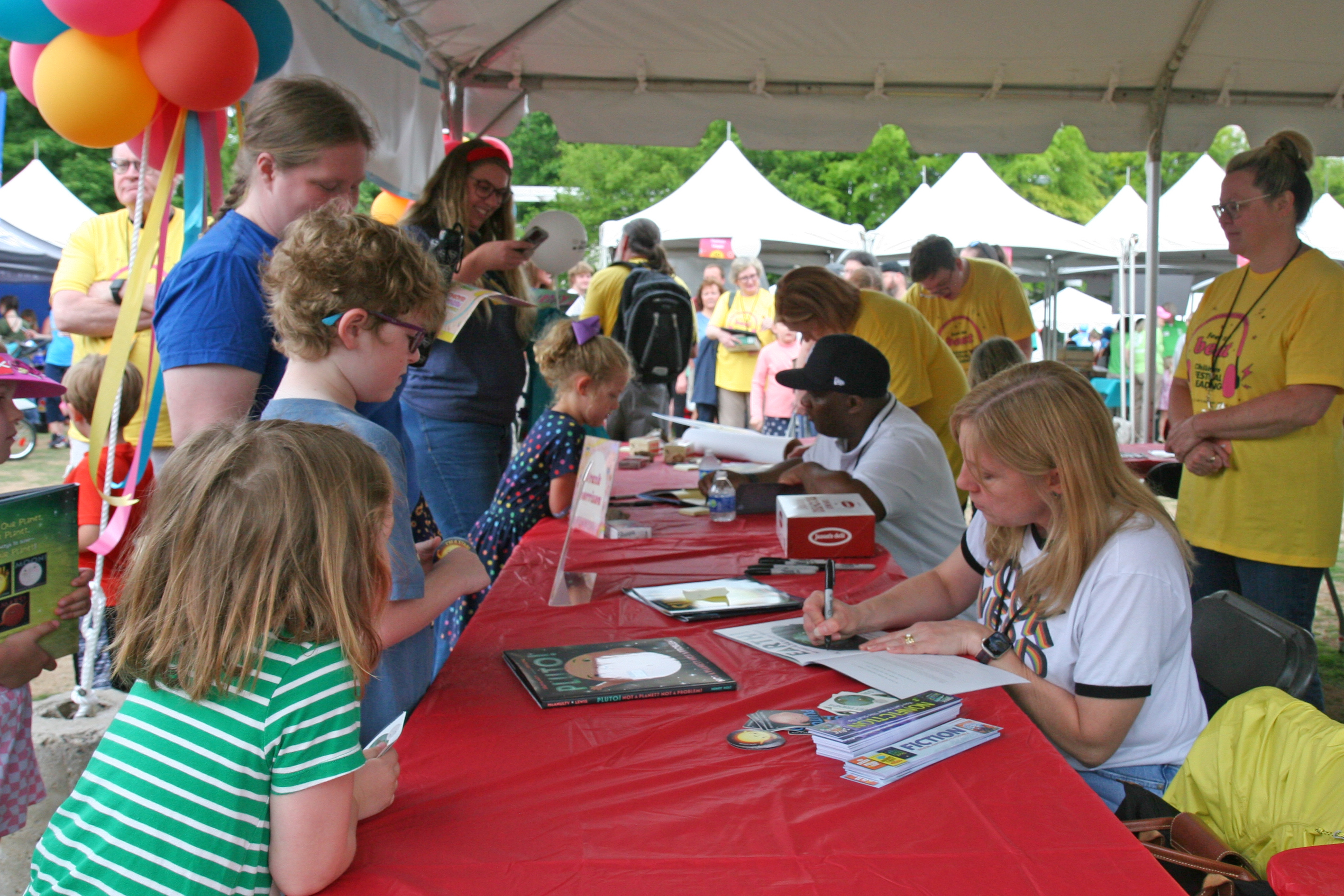 Photo of authors signing books at a table as kids look on