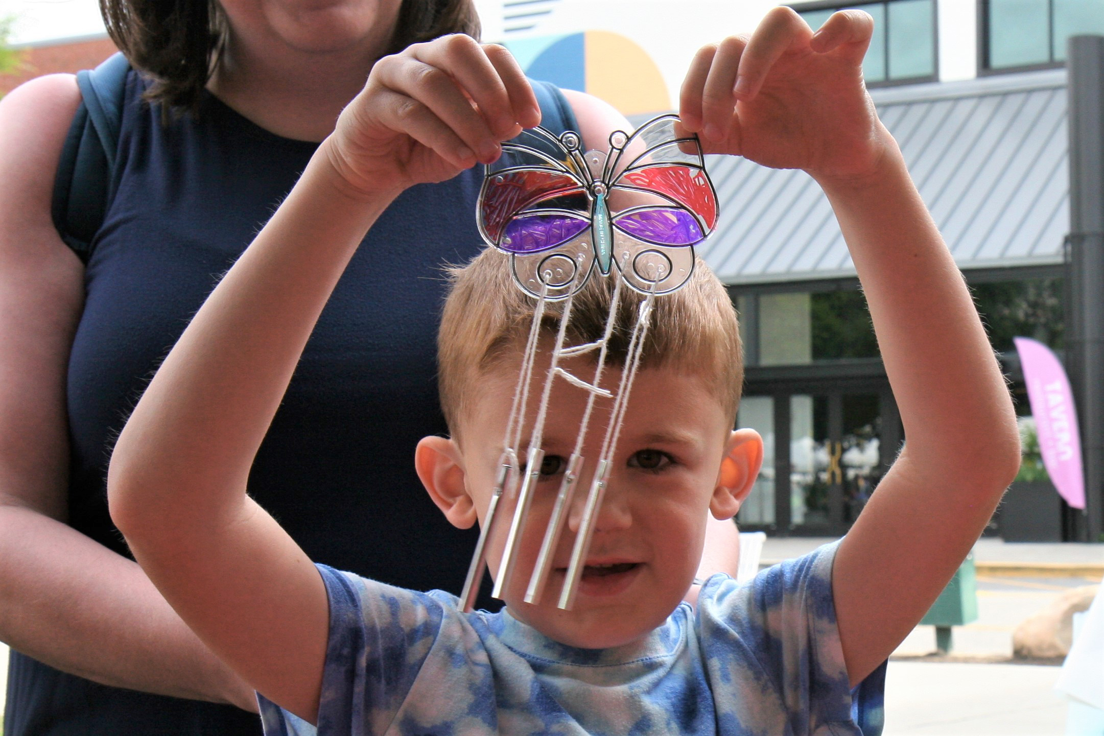 Young boy holds up a small butterfly windchime he crafted