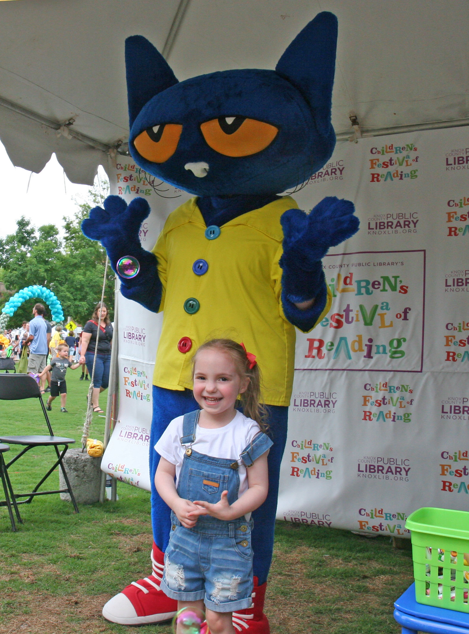 Little girl smiles in front of Pete the Cat costume character