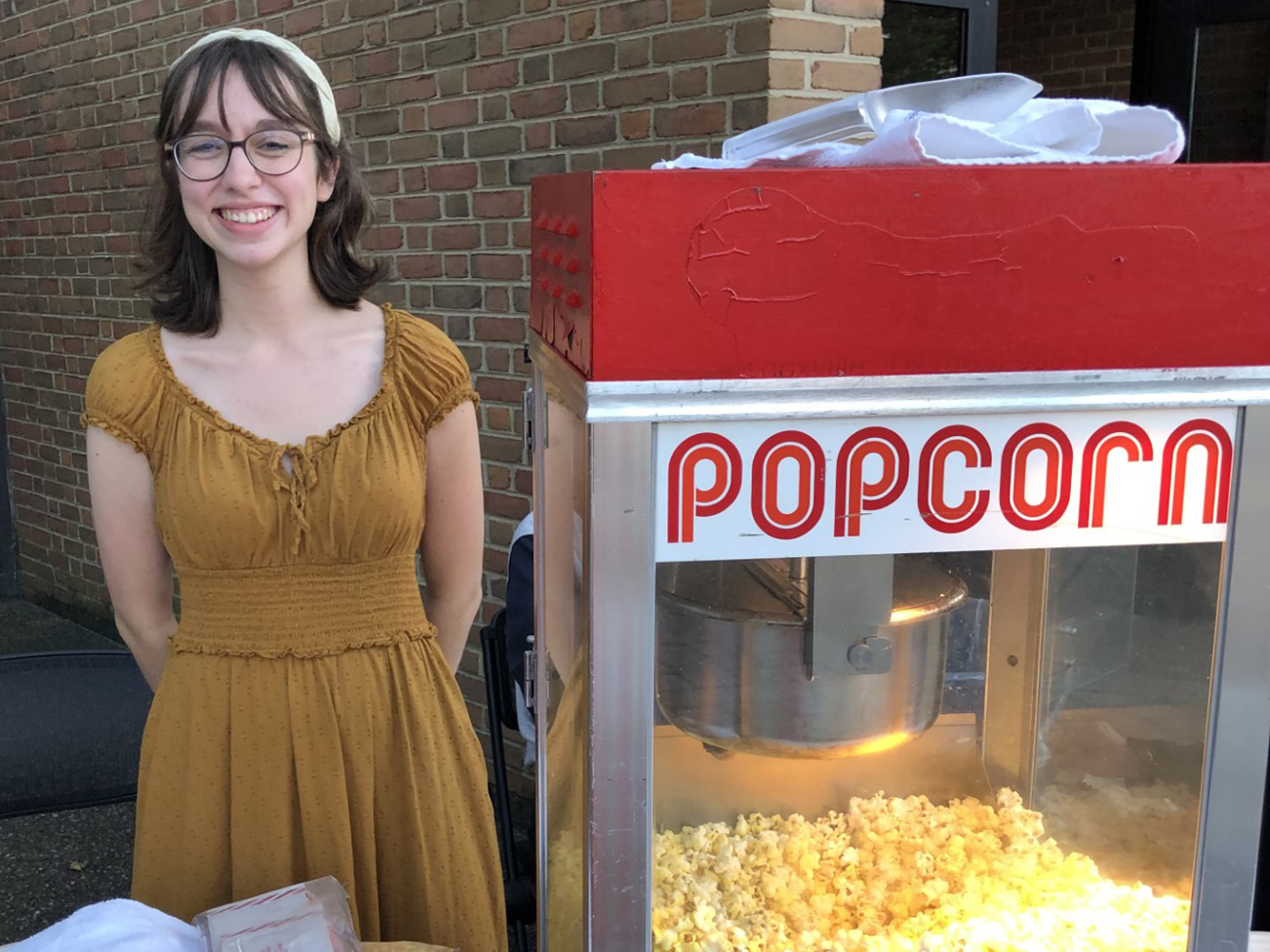 young woman smiles next to a theater popcorn machine
