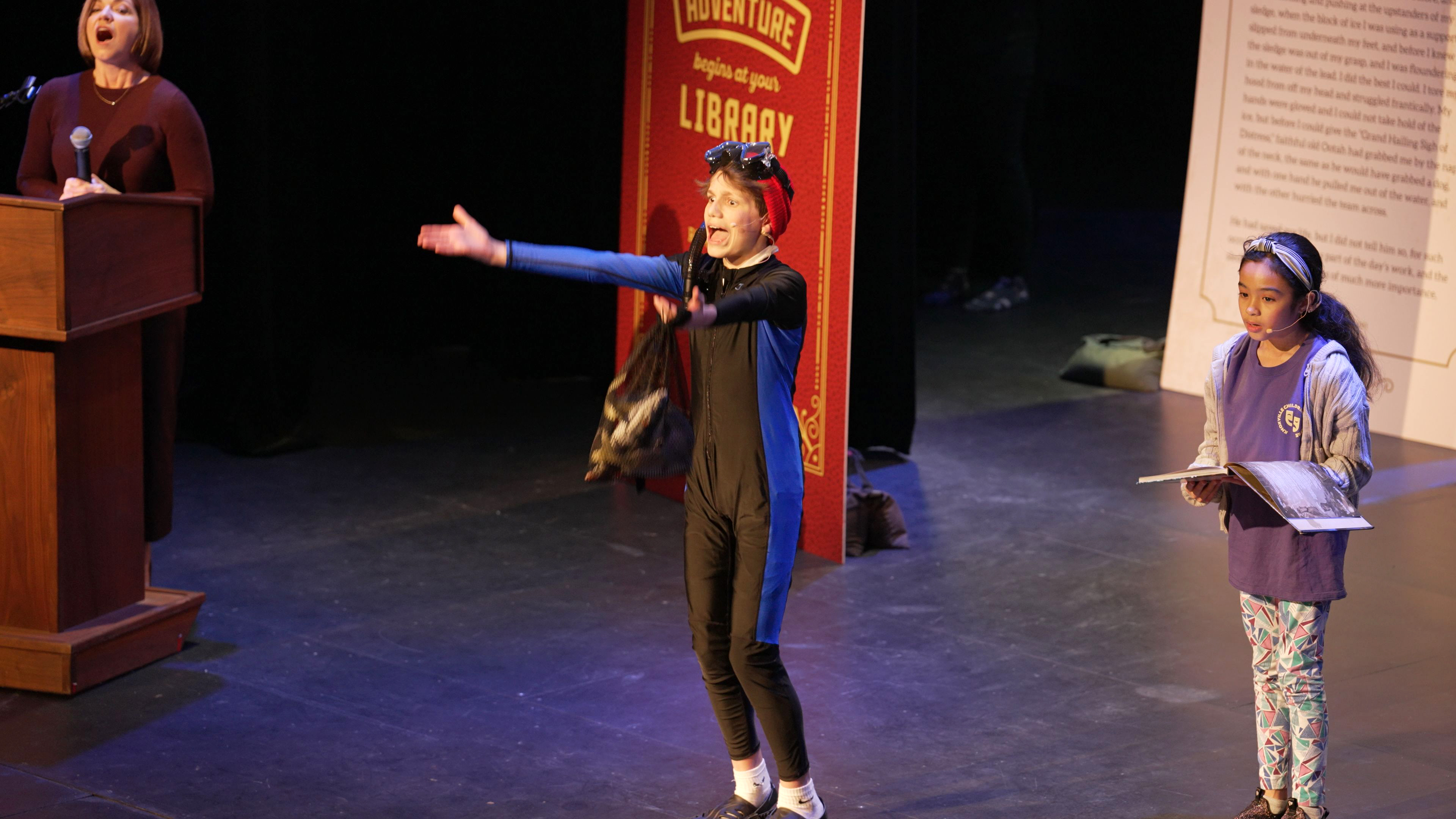 young actor on stage dressed in a scuba costume with young girl holding an open book