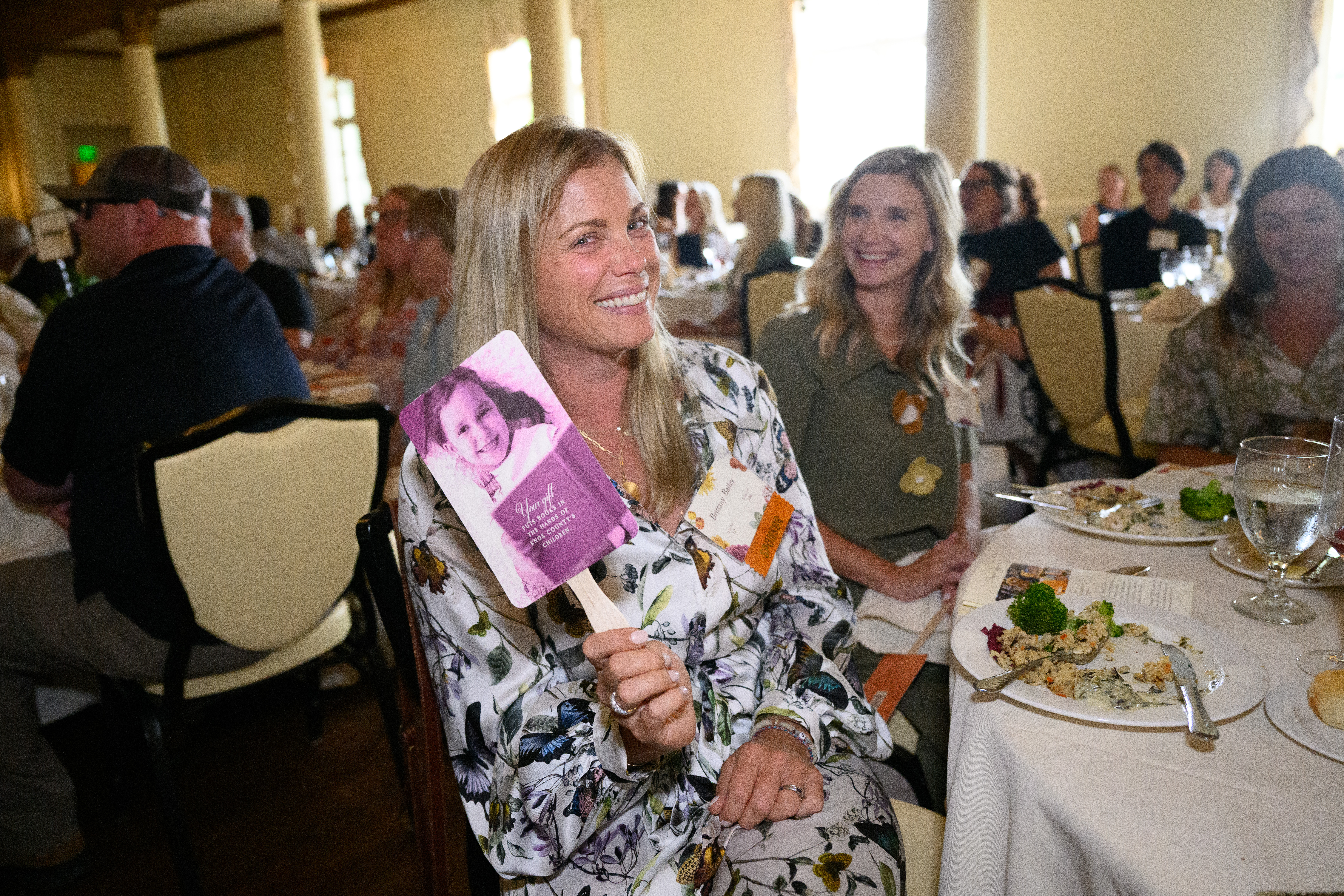 A woman smiles and holds a purple poster for the camera
