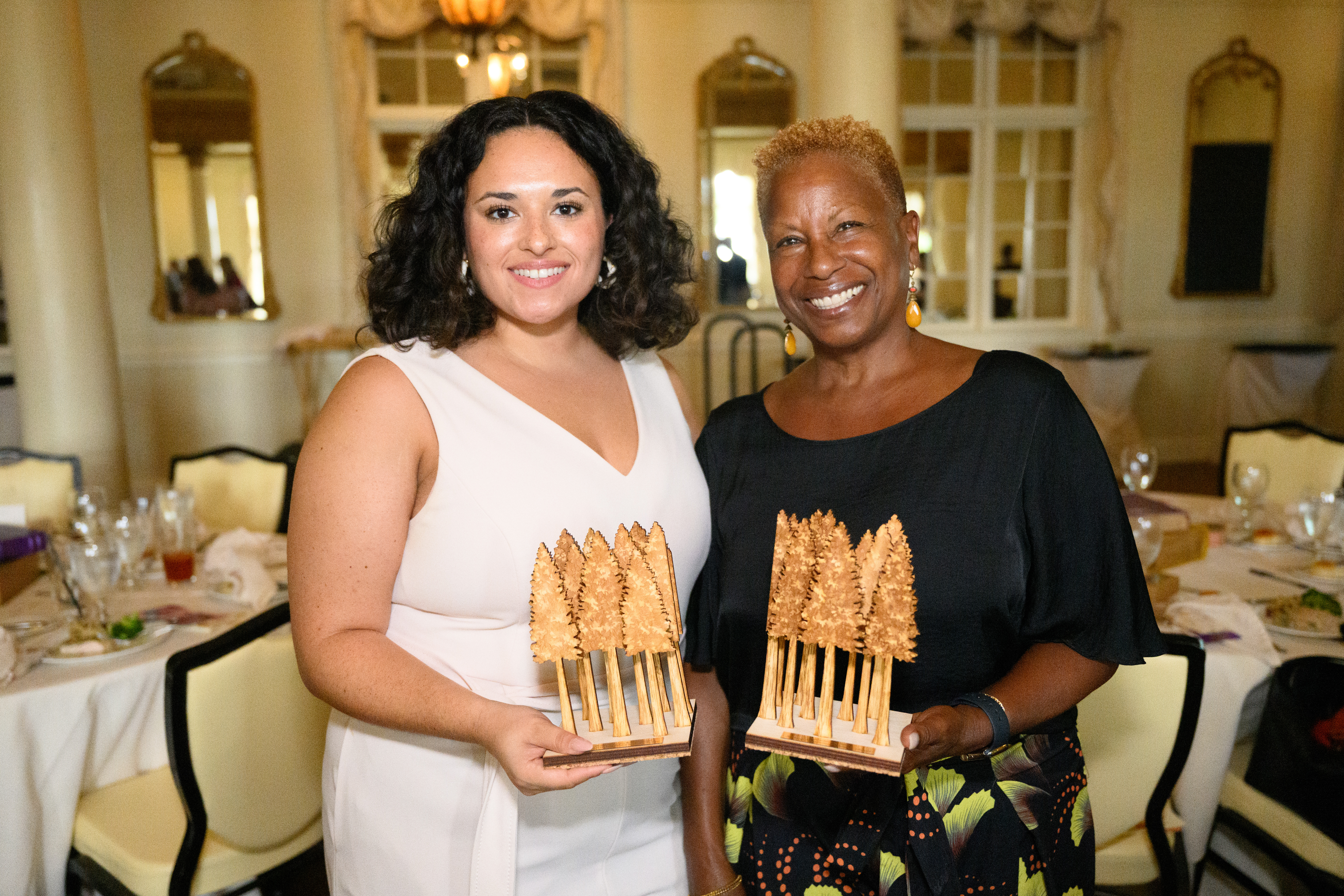 Two smiling women holding two halves of a plaque of trees
