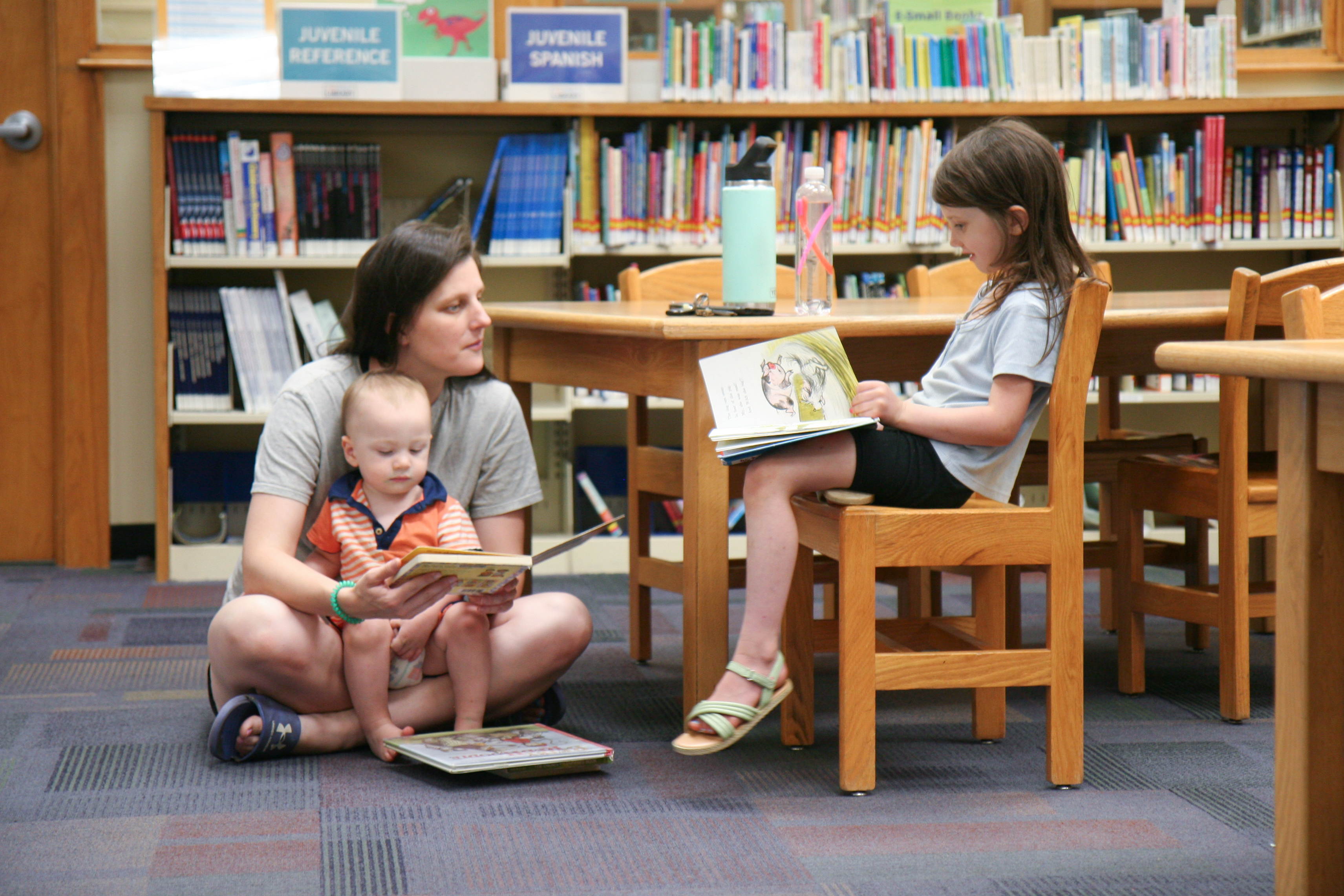 photo of mom and two children reading in a library