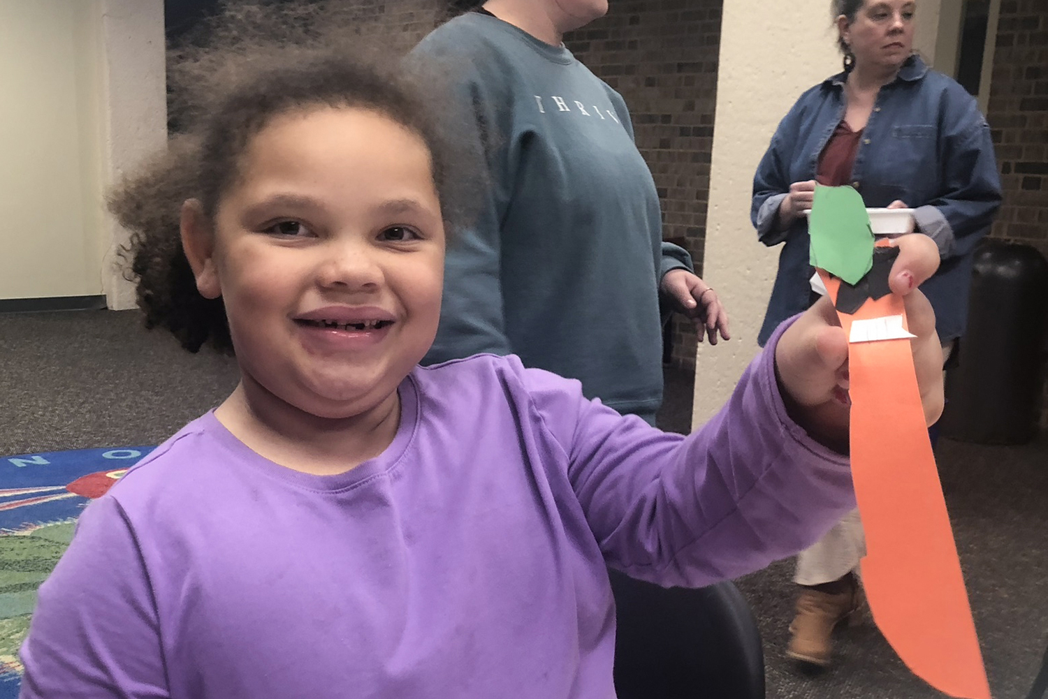 girl smiles and holds up a craft