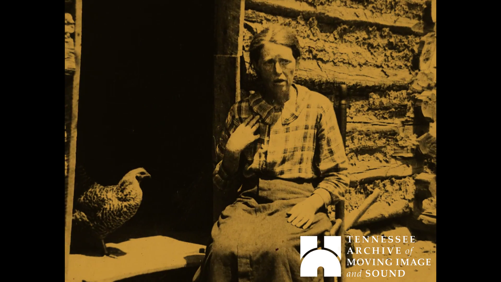 A woman sitting by cabin with a hen in the doorway