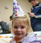 preschool girl wearing a paper party hat reading "Happy Birthday Dolly""