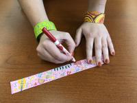photo of woman coloring a paper bracelet while wearing one on each wrist