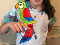 colorful paper parrot balancing on young girl's finger
