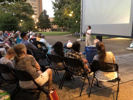 woman addresses outdoor crowd in front of large screen