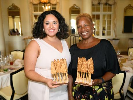 Two smiling women holding two halves of a plaque of trees
