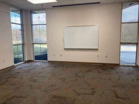 Photo shows carpeted room with blinds on windows, dry-erase board, projection screen, wall outlets.