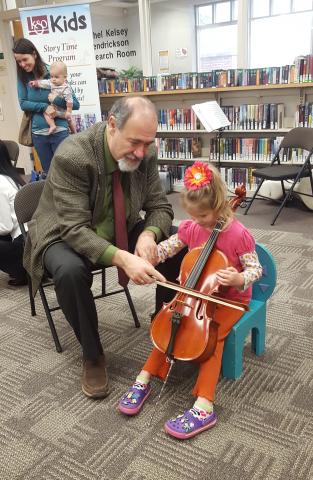 Man helps a young girl play a violin