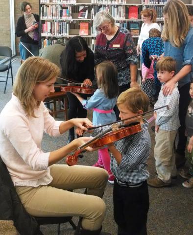 photo of a woman helping a young boy hold and play a violin
