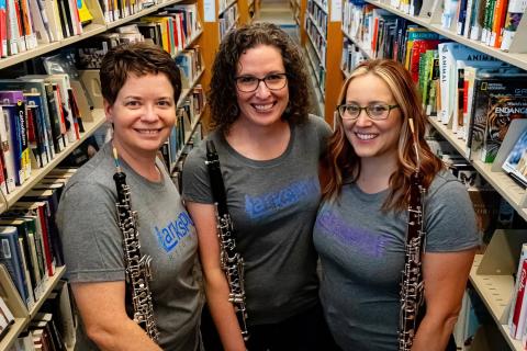 Three women musicians holding woodwind instruments in a library