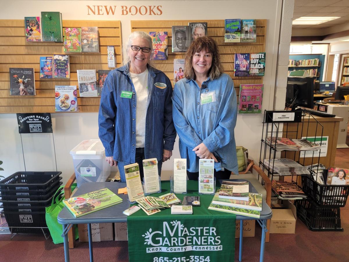 two ladies stand and smile behind a table with Master Gardeners Knox County Tennessee banner