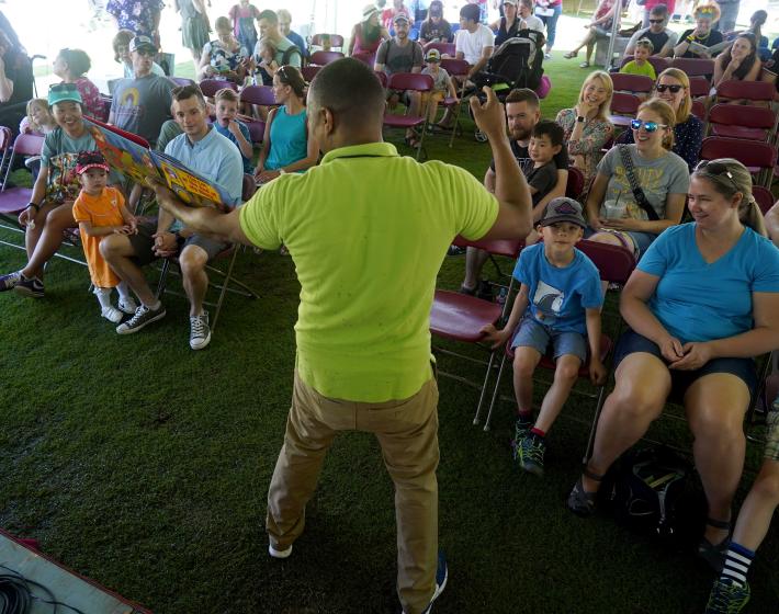 Person in green shirt speaking in front of a group at the Children's Festival of Reading 2019.