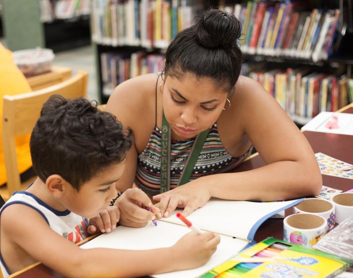 Young boy receiving homework help from woman at the library