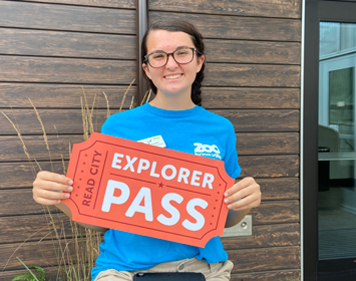 Young woman holds an oversized ticket that reads Read City Explorer Pass
