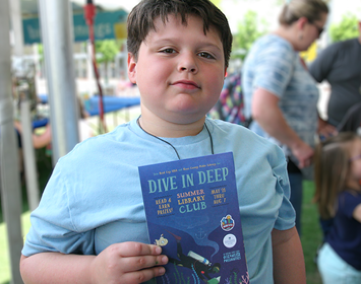 Photo of a boy holding a folded blue map that reads Dive in Deep