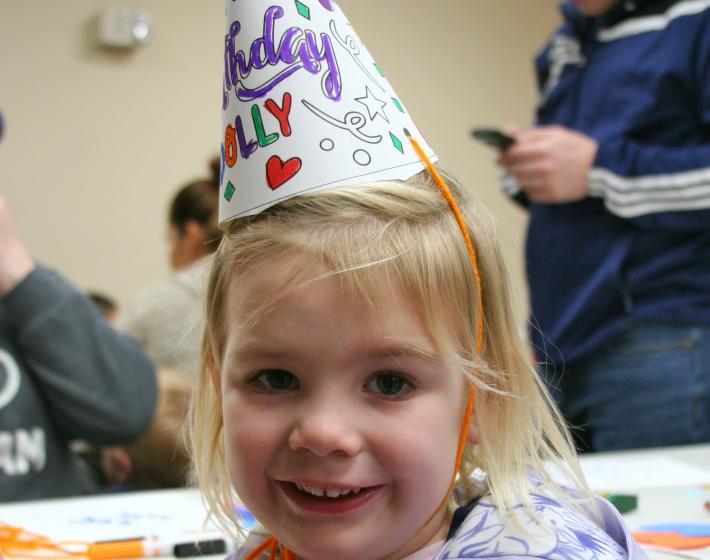preschool girl wearing a paper party hat reading "Happy Birthday Dolly""