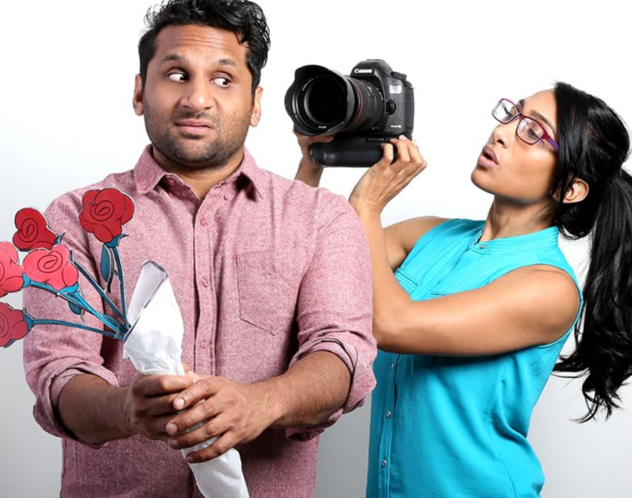 photo of Indian-American man holding flowers and making skeptical face as a woman films him with a camera