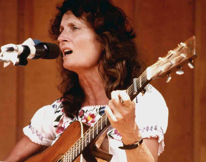 photo of Alice Gerrard playing guitar at a microphone ca 1960s
