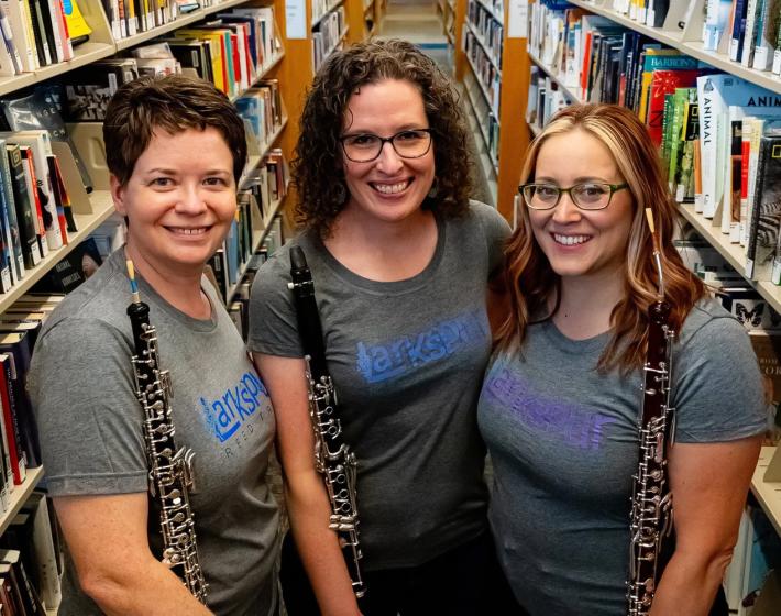 three women hold woodwind instruments in a library 
